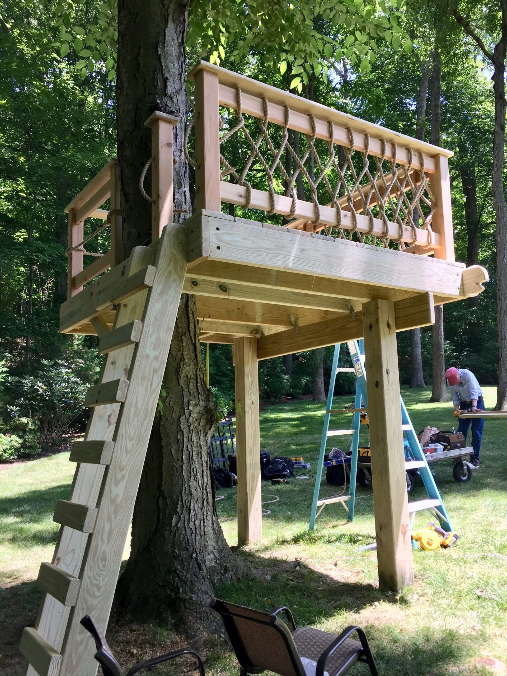 Wooden treehouse with rope railing being constructed in backyard