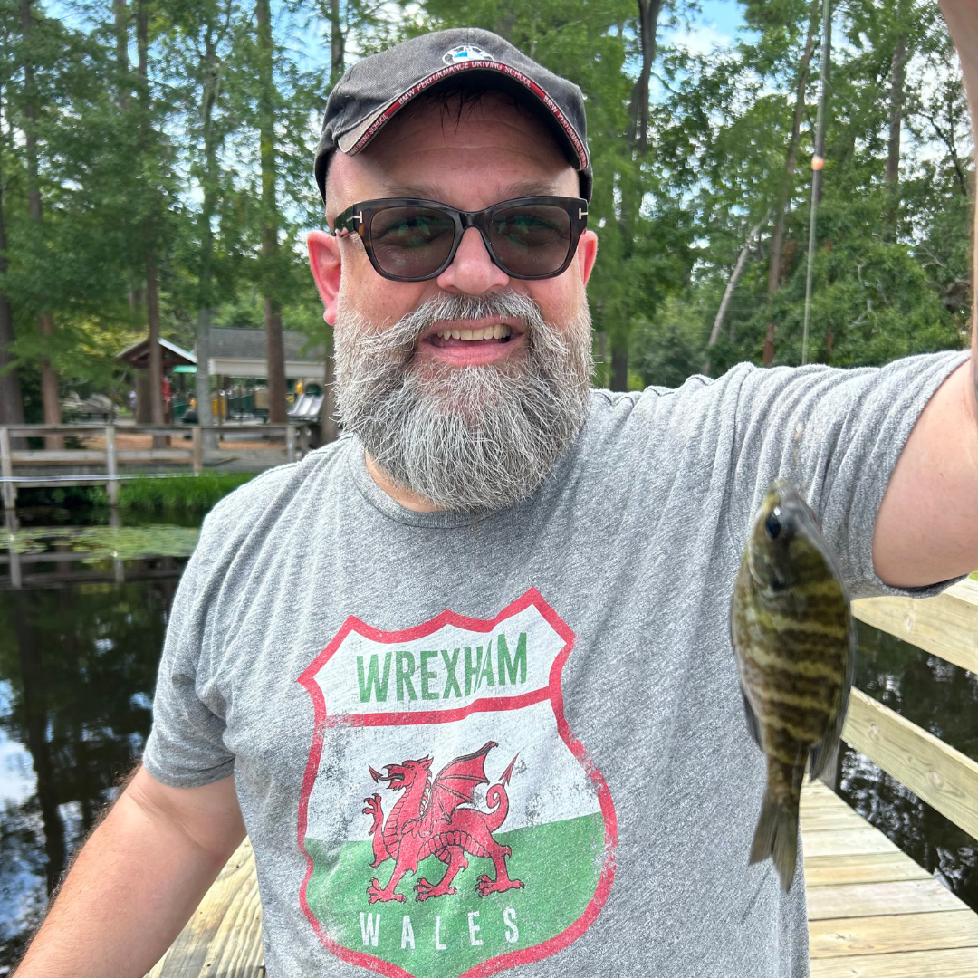 Smiling man in Wrexham Wales shirt holding fish on wooden dock