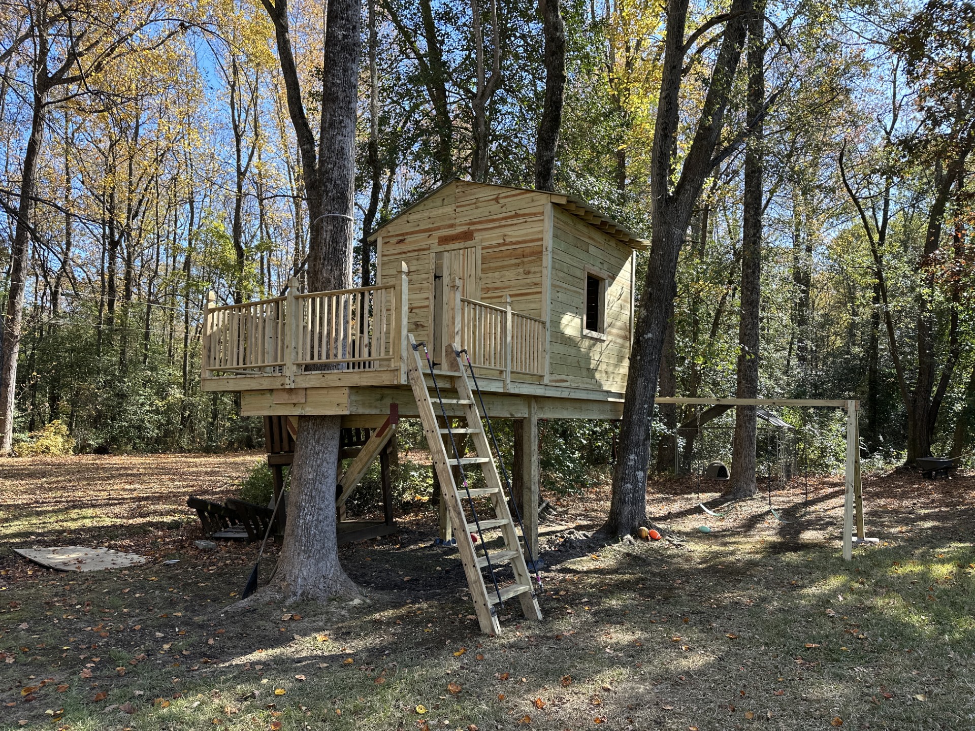 Finished cabin-style treehouse built around a tree with a ladder up to the deck