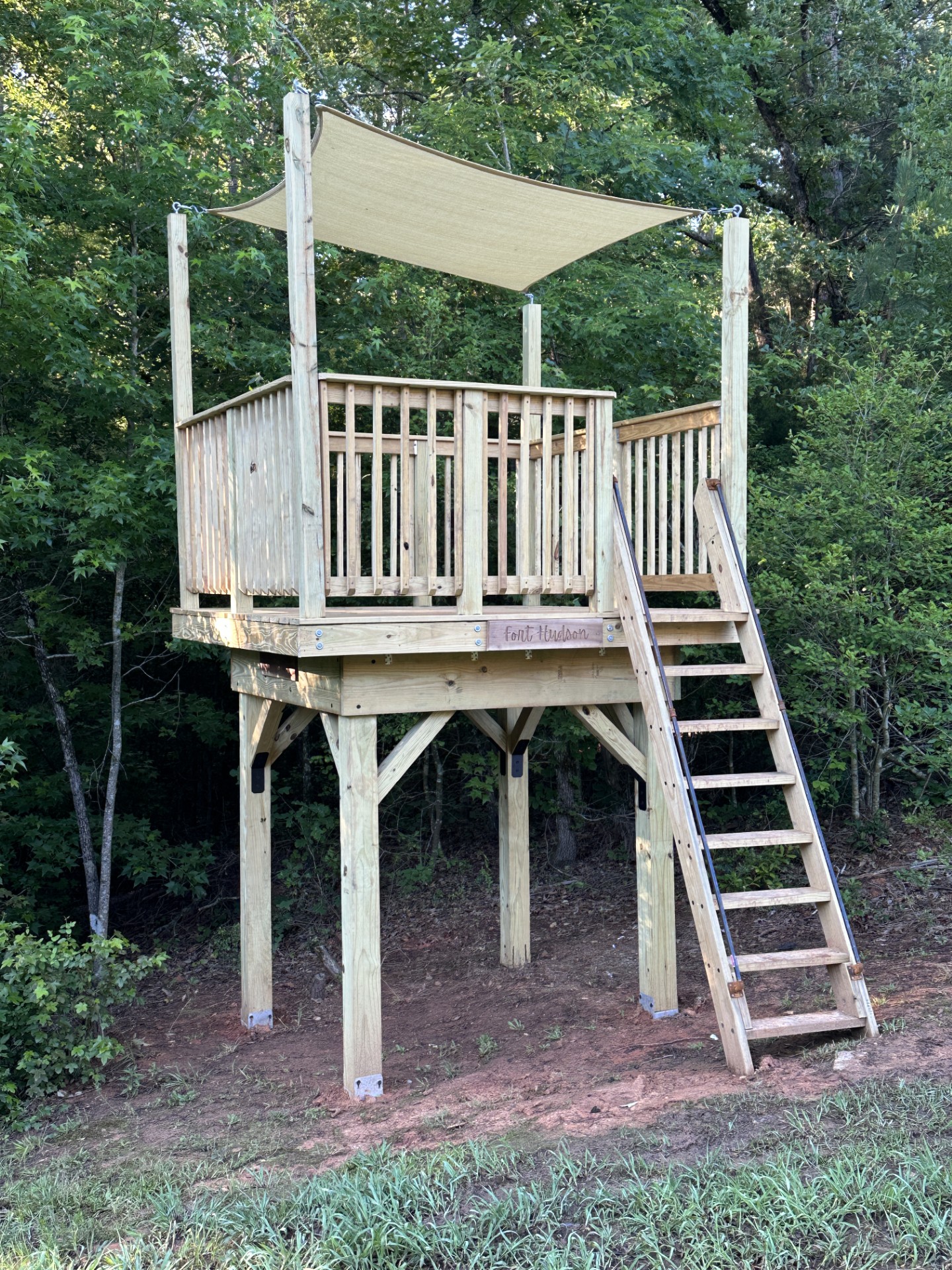 Post-supported backyard fort with a shade sail and a wide stair, built at the treeline
