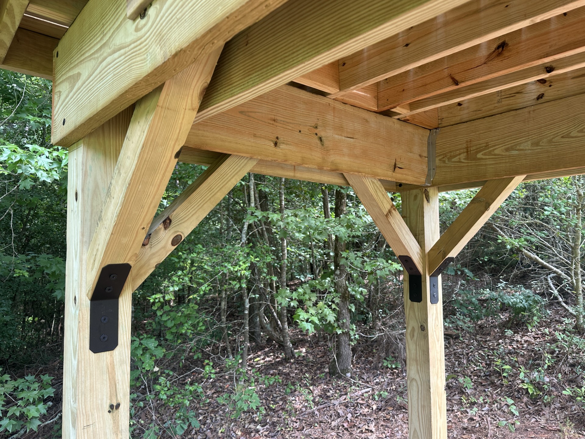 Underside of a treehouse platform showing the beams, joists, knee braces and steel brackets