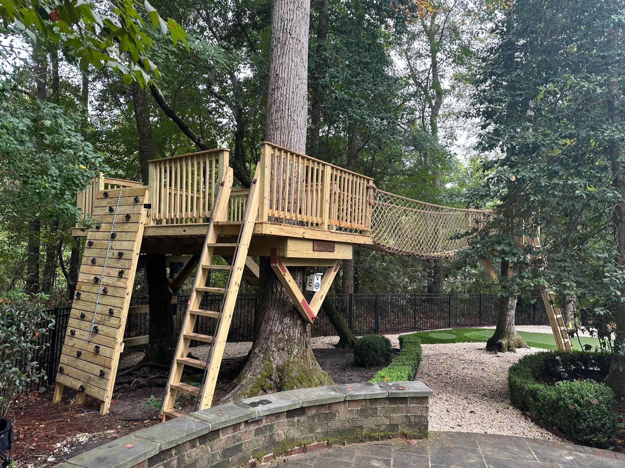 Custom treehouse platform built around a large tree with a climbing wall, ladder and rope net bridge