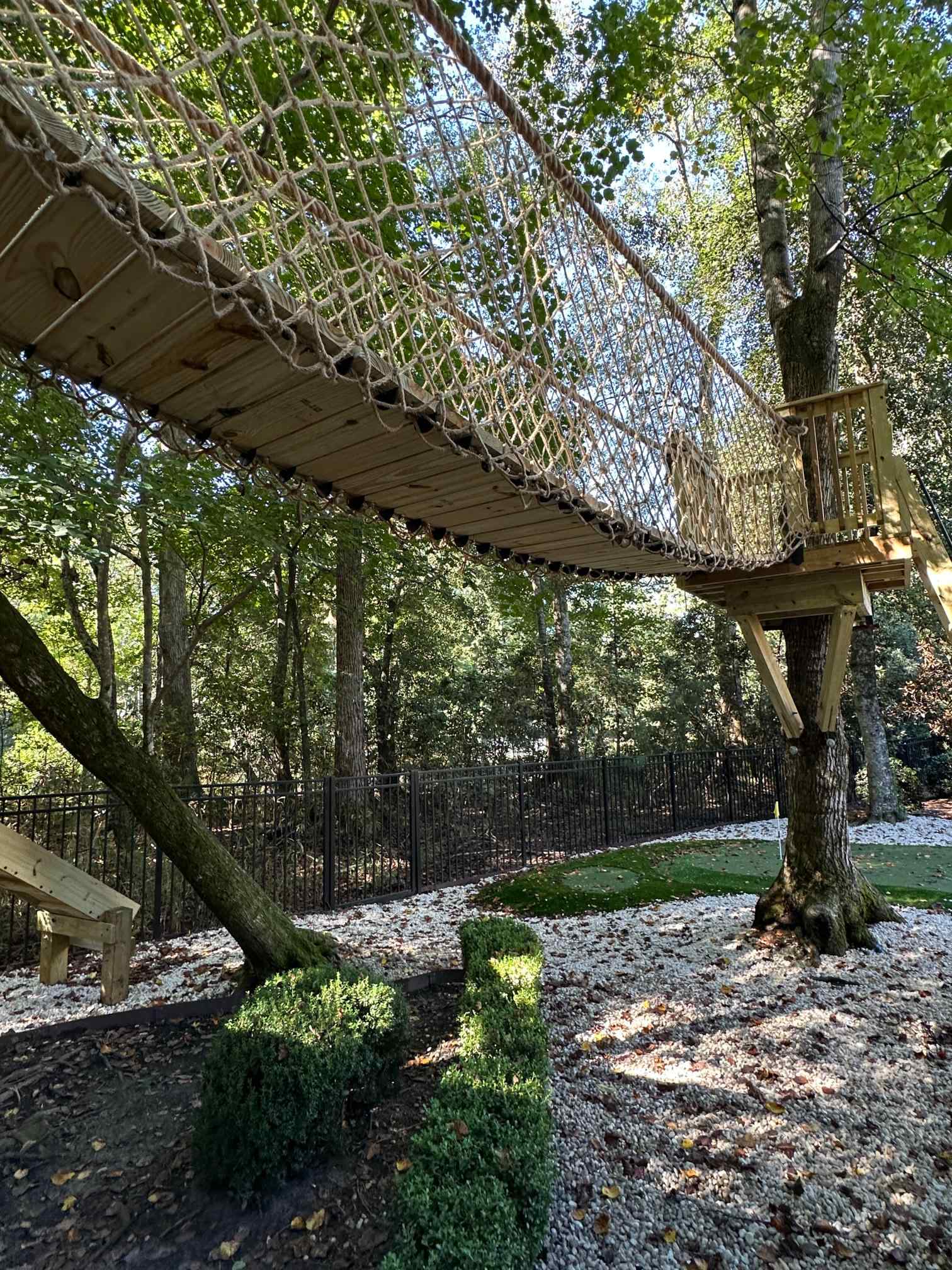Rope net suspension bridge spanning between two treehouse platforms, seen from below